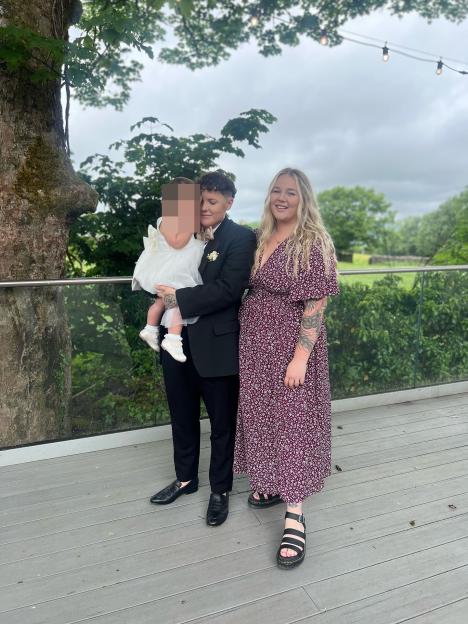 A parent holding two children, one an infant and the other a toddler, in a hospital bed.