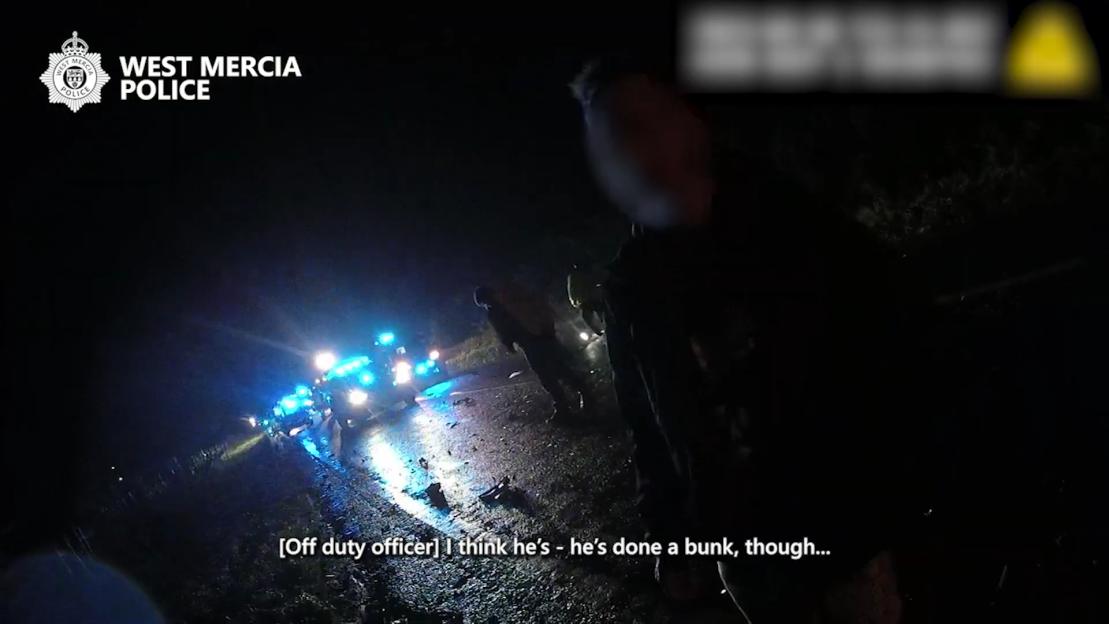Police at a crash scene at night, with flashing blue lights reflecting on the wet road.