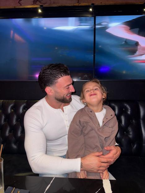 Jake Quickenden smiling and holding his son, Leo, who is making a funny face.