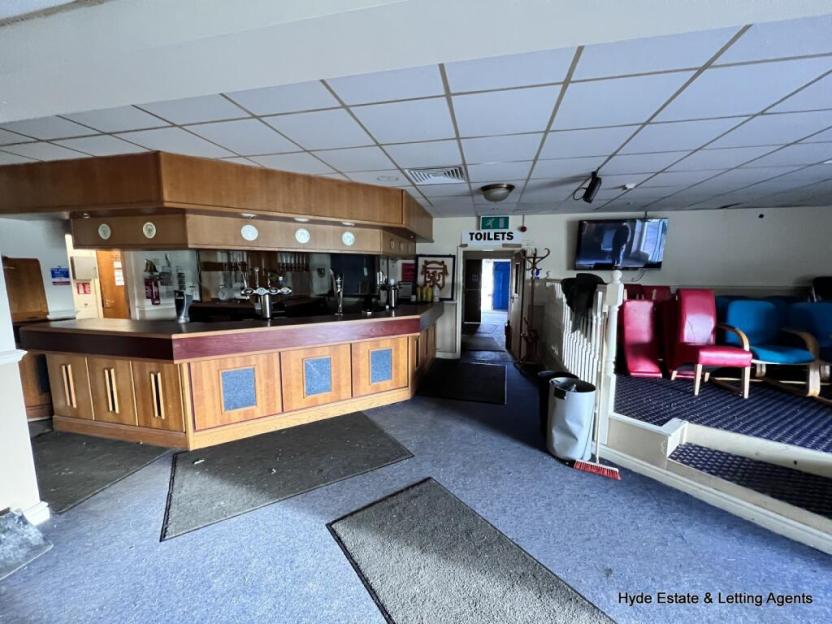Interior of a bar with a wooden bar counter, seating area, and a television.