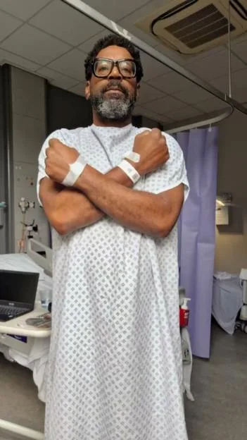 Kevin Mathurin in a hospital gown with arms crossed.