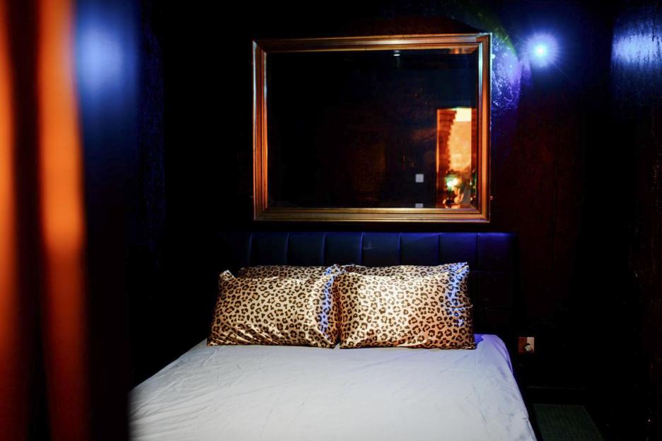 A bed with leopard print pillows and a mirror above it, in a dimly lit room with blue and orange lighting.