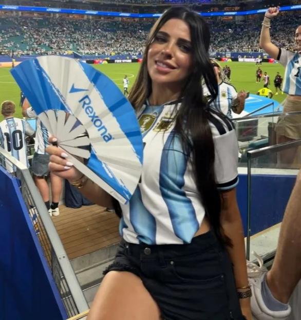 A woman in an Argentina soccer jersey holds a "Rexona" branded fan at a stadium.