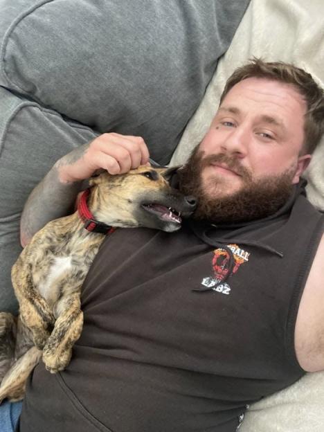 A man with a beard lying down and petting a brindle dog.