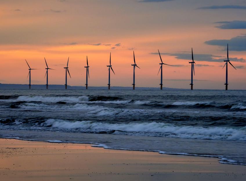 Wind turbines at Marske, North Yorkshire Coast, silhouetted against an orange and yellow sunset with waves breaking on the shore.
