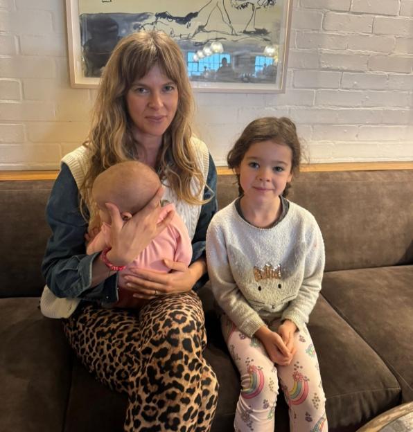 Woman in leopard print pants holding a baby and sitting next to a young girl.