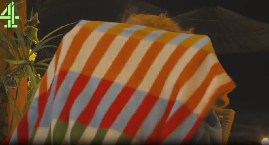 A person with orange hair covered by a striped blanket.