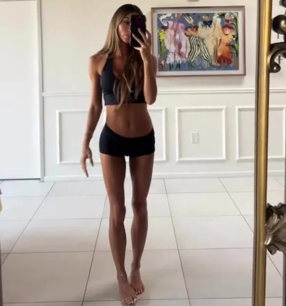 A woman in a black sports bra and shorts takes a mirror selfie.