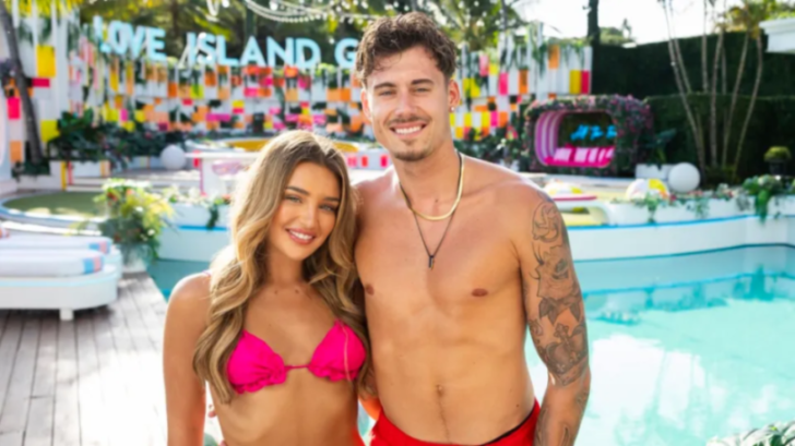 A smiling couple posing outdoors, with a pool and a "Love Island" sign in the background.