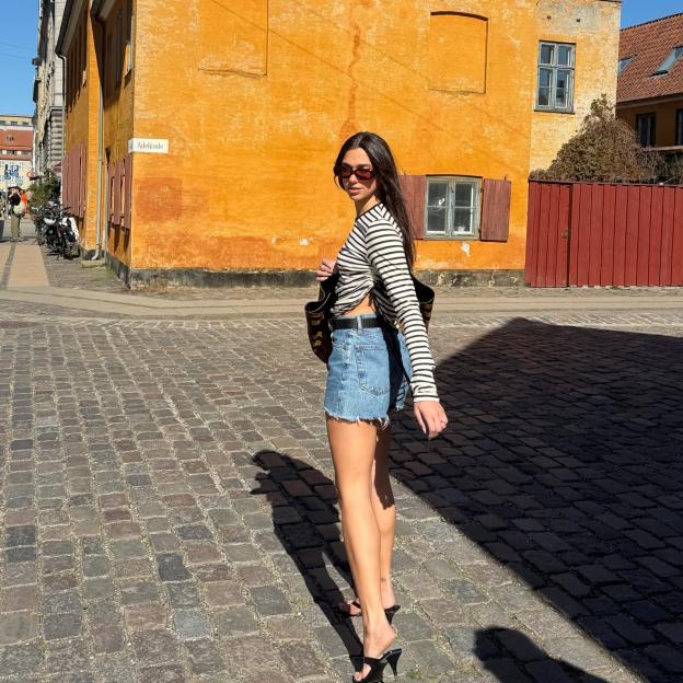 Dua Lipa in Copenhagen, standing on a cobblestone street in front of a yellow building.