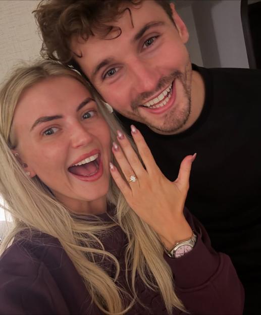 Lucy Fallon and her partner smiling, with Fallon holding up her hand to show off her engagement ring.