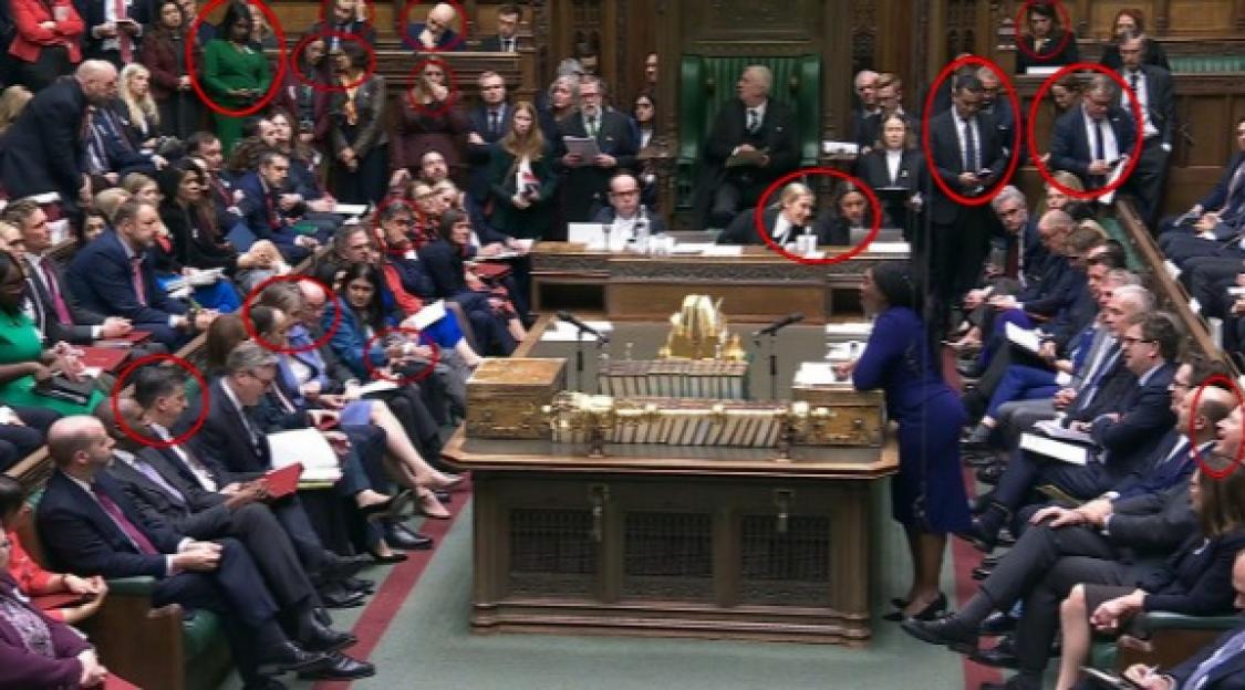 People in a parliament or assembly, some looking at their phones.