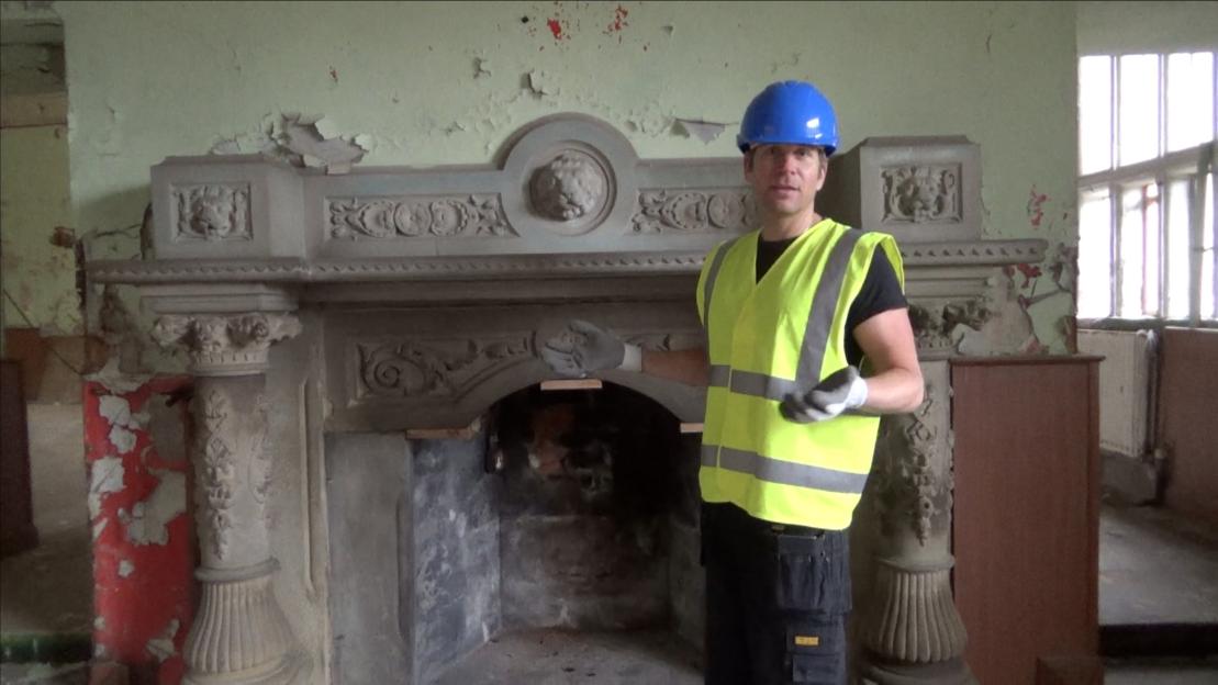 Hopwood DePree in a hard hat and safety vest standing in front of a dilapidated fireplace at Hopwood Hall.