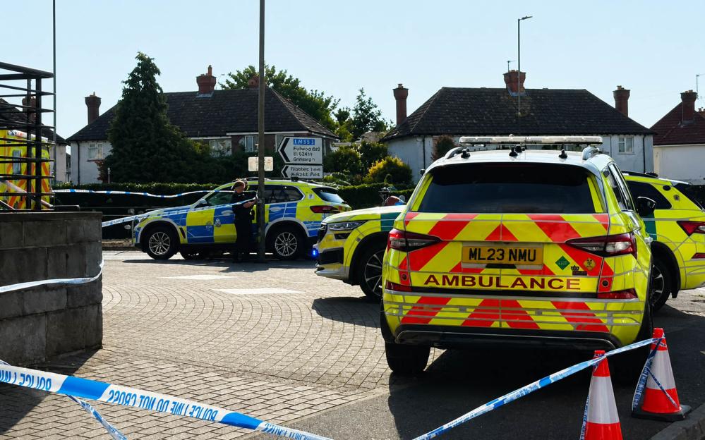 Police and ambulance vehicles at a crime scene blocked off with police tape.