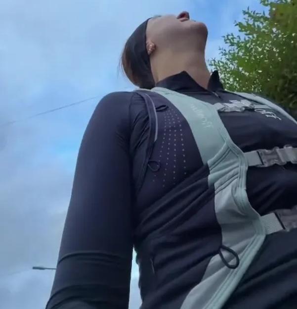 A person looks up at the sky, wearing a dark long-sleeved athletic top and a hydration vest.