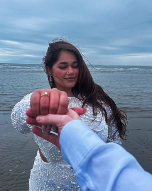 A woman in an embroidered dress holding hands with a man on a beach.