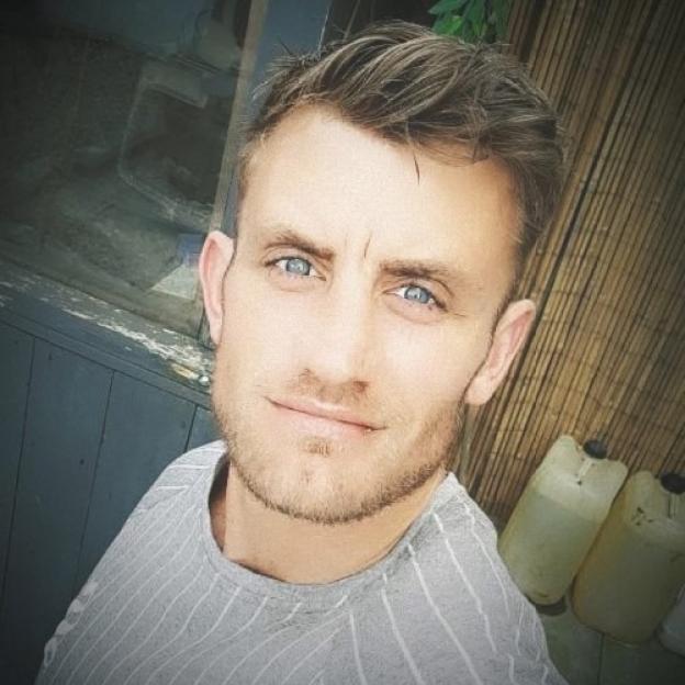 Paul Stewart Miller, a man with light brown hair, blue eyes, and a light beard, smiles faintly.