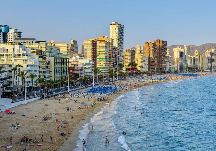 View of Benidorm beach in Spain, with people on the sand and in the water, and tall buildings along the coastline.