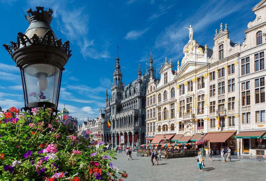 Brussels Grand Place with ornate buildings, a street lamp with flowers, and people.