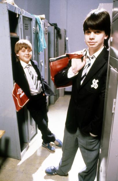 Two pupils in uniform, George Christopher and John Alford, standing near school lockers from the TV show Grange Hill.