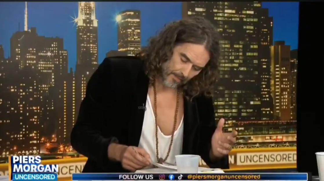 Russell Brand looking down at papers in front of him during an interview on Piers Morgan Uncensored.