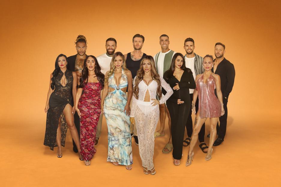 A group of 12 people, six men and six women, posing together in front of an orange background.