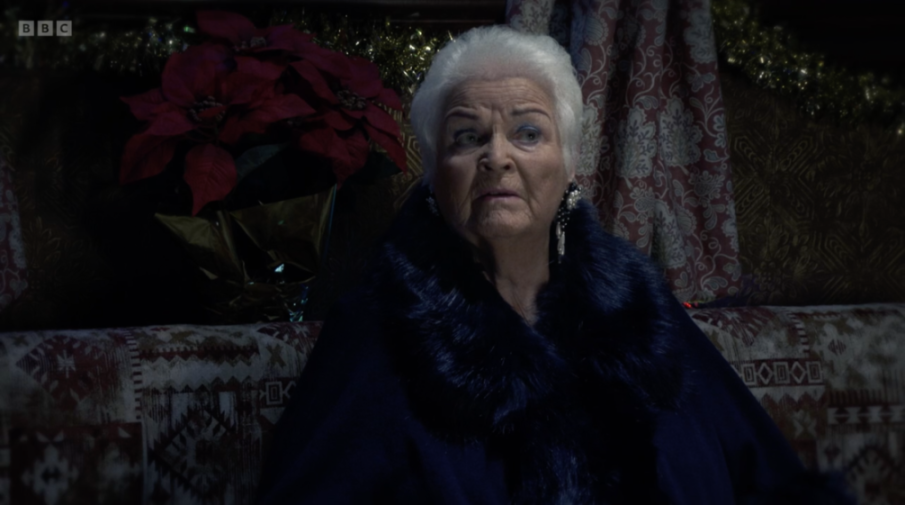 An older woman with white hair and a blue fur coat looking to the right.