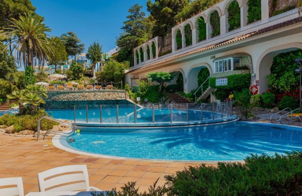 A resort swimming pool with a terraced building and lush greenery.