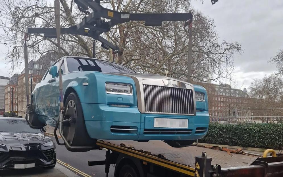 A light blue Rolls-Royce being towed onto a flatbed with a black Lamborghini parked nearby.