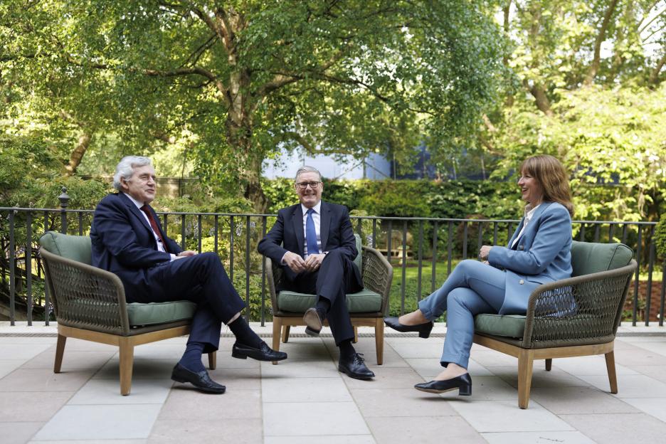 Prime Minister Keir Starmer, Gordon Brown, and a woman seated outdoors in conversation.