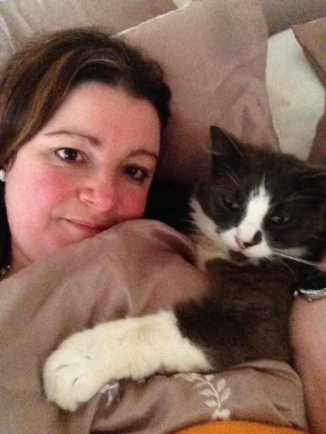 A woman in bed taking a selfie with her cat, Walty.