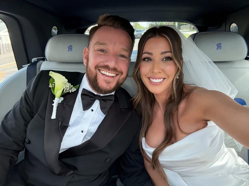 Jamie O'Hara and Keziah Grubb smiling in a car on their wedding day.