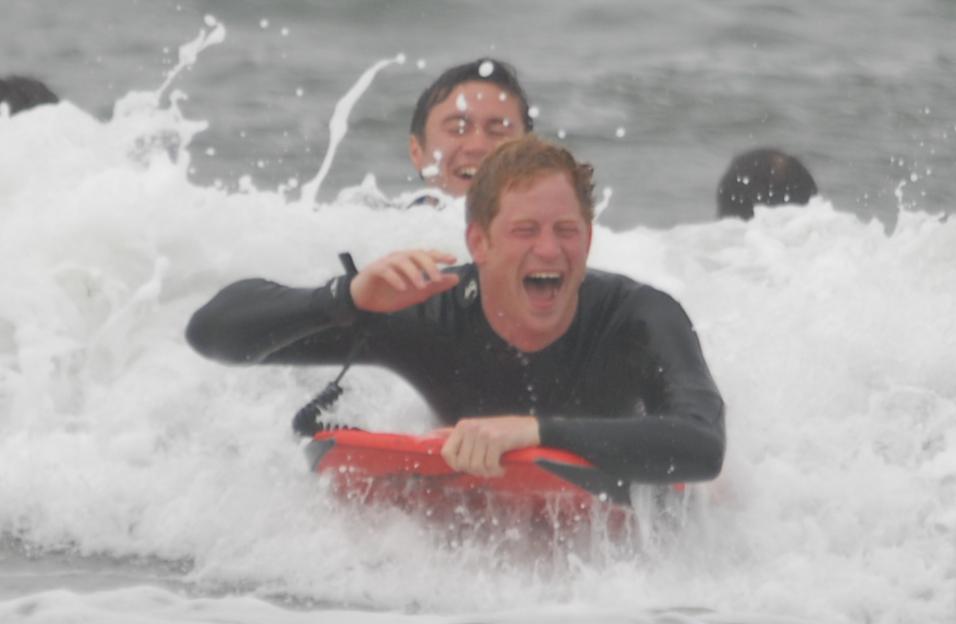 Prince Harry bodyboarding in the ocean while Prince William is seen behind him, also in the water.