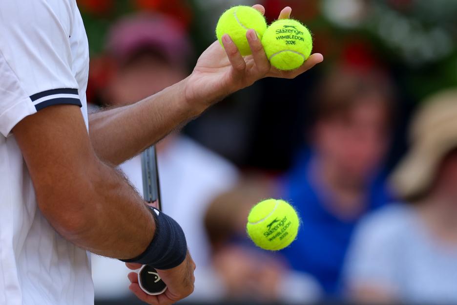 A tennis player holds two tennis balls, with a third one falling, all labeled "Slazenger Wimbledon 2026."