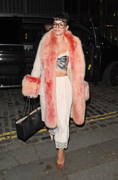 Lilly Allen in a pink fur-lined coat, silver sequined crop top, silk trousers, and glasses, carrying a black Chanel handbag.