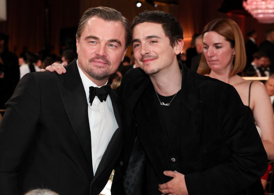 Leonardo DiCaprio in a tuxedo and Timothée Chalamet in a dark velvet suit posing together at the 83rd Golden Globe Awards.