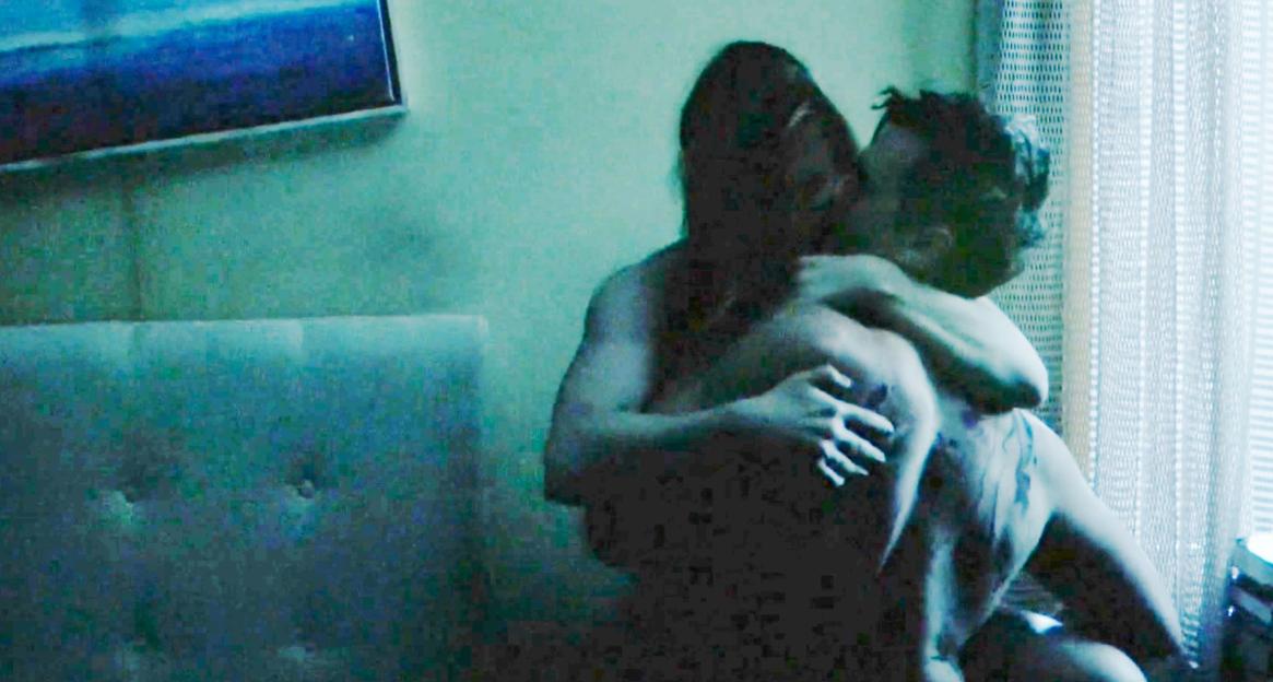 Two people embrace intimately in a dimly lit room.