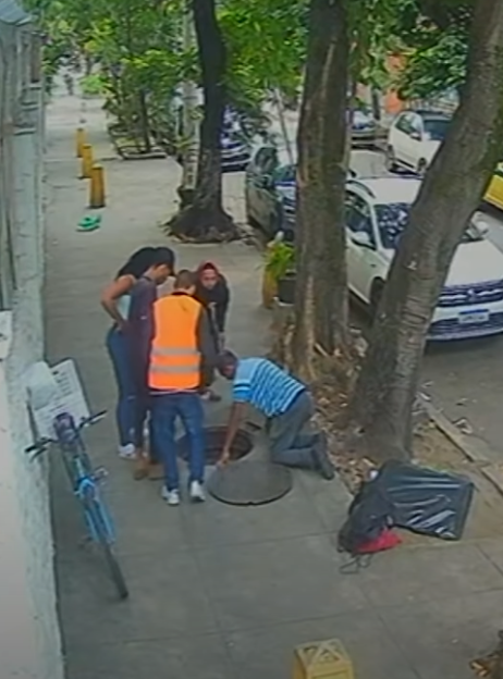 Several people looking into an open manhole cover on a sidewalk.
