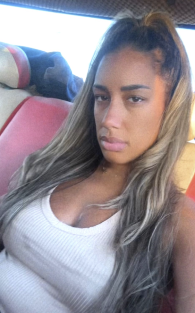 A young woman with long, highlighted hair wearing a white tank top.