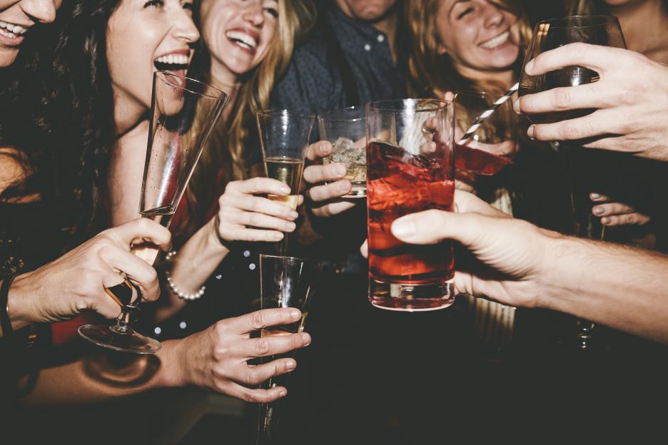 Group of adults toasting and laughing with cocktails and champagne.