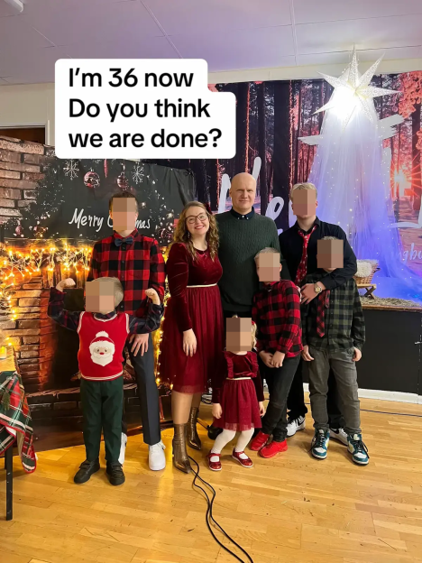 A family of eight, including a woman and a man and six children, stand together in front of a holiday backdrop.