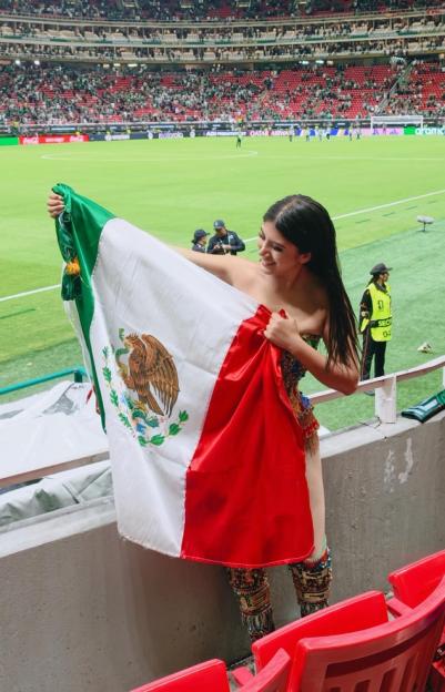 A screenshot of an Instagram post featuring a woman holding a Mexican flag in a stadium.