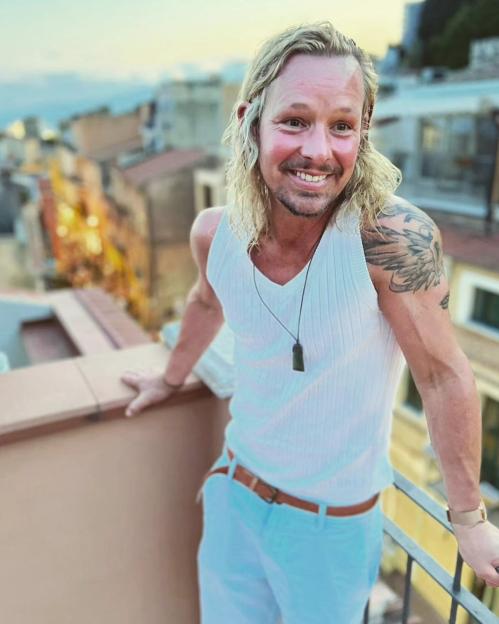 Adam Rickitt with a new look, smiling on a balcony.