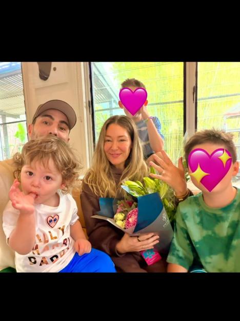 Erin Mcnaught with her fiancé and three children, holding two bouquets of flowers and showing her engagement ring.