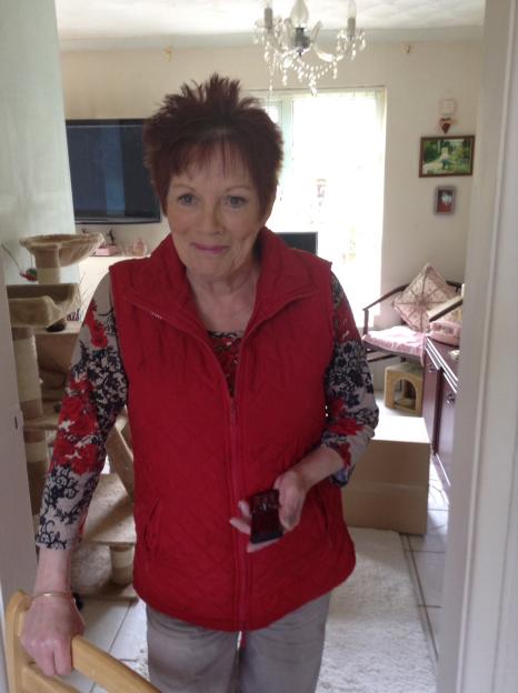 Anne Hughes, a 71-year-old woman involved in a newsagents' shutter accident, stands indoors wearing a red vest and a floral long-sleeved shirt.
