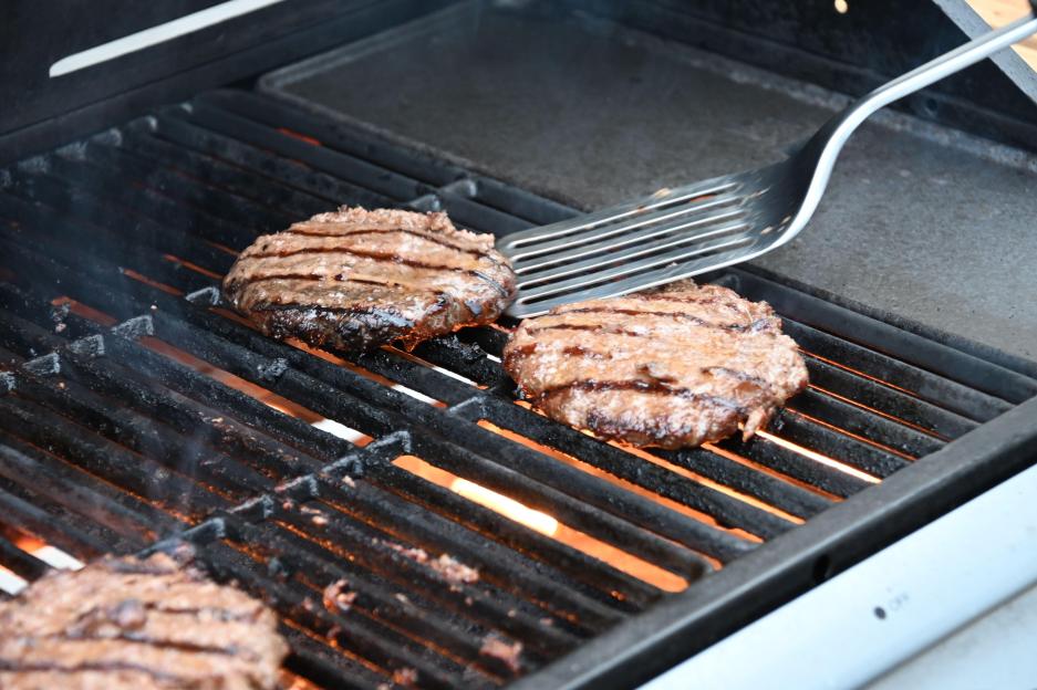 Flamed grilled beef burgers barbecued on an outdoor BBQ with a spatula.