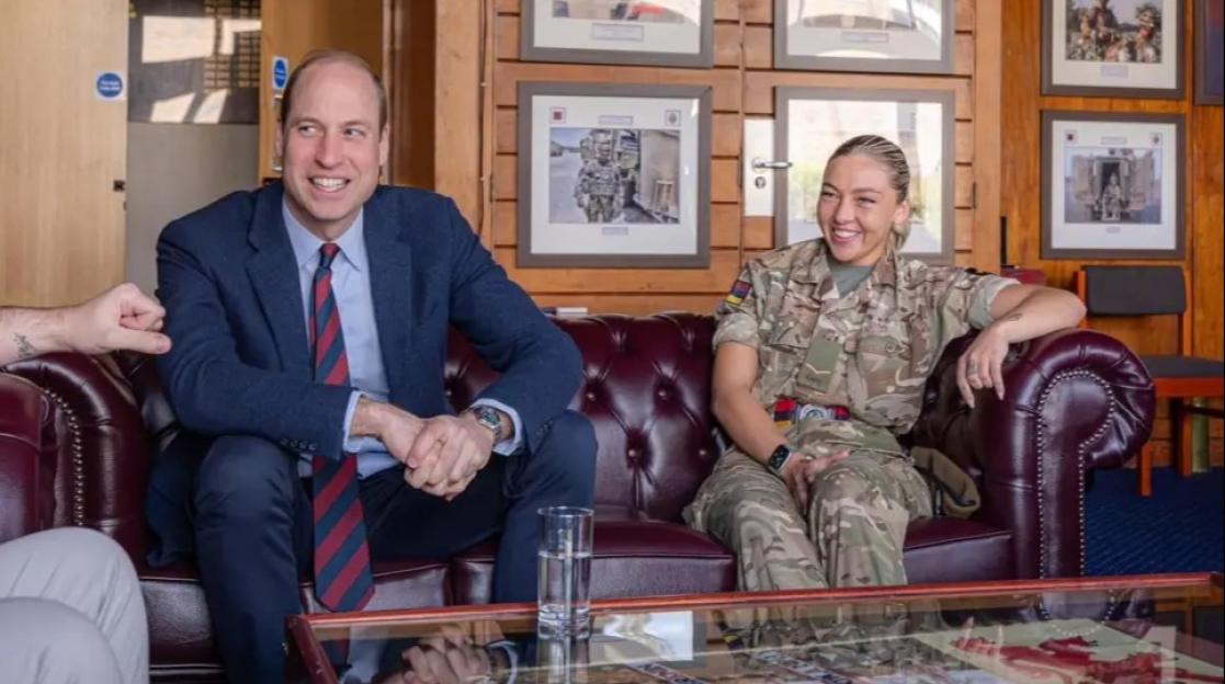 Lucy Wilde, in military uniform, laughing with Prince William on a leather couch.
