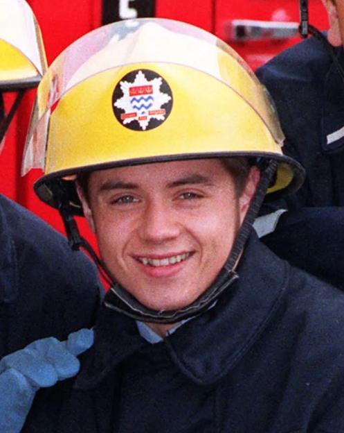 John Alford, who plays fireman Billy Ray in London's Burning, wearing a yellow fireman's helmet.