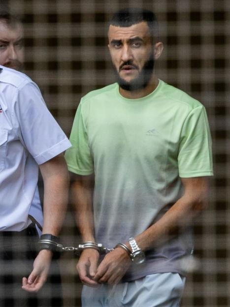Abdulla Ahmadi, handcuffed and wearing a light green shirt, leaving Hove Trial Centre with a guard.