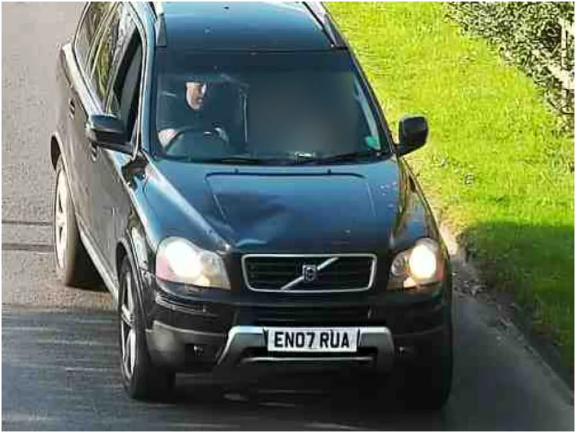 A black Volvo XC90 drives on a road next to grass.